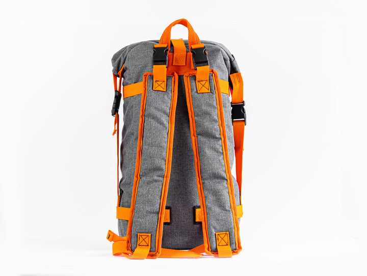 Rear view of the Grava Backpack where the handmade quality of the shoulder straps are shown.  The shoulder straps are outlined with an orange fabric but still using the grey canvas material for the majority of the shoulder braces.  There is also a good view of the orange top strap for easy hand carry functions.
