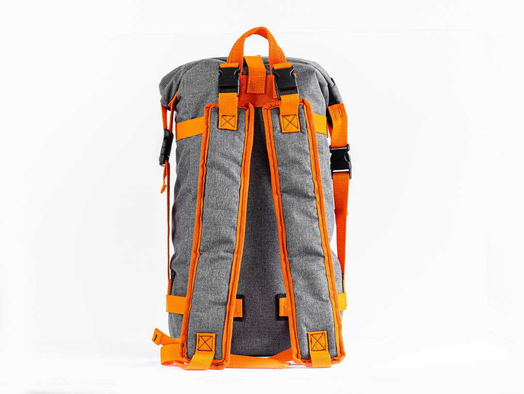Rear view of the Grava Backpack where the handmade quality of the shoulder straps are shown.  The shoulder straps are outlined with an orange fabric but still using the grey canvas material for the majority of the shoulder braces.  There is also a good view of the orange top strap for easy hand carry functions. 
