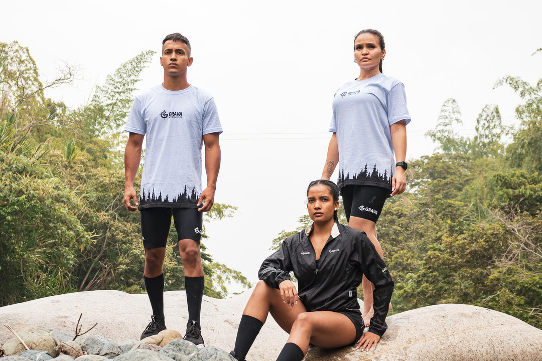 Two women and a man, wearing the Grava Mountain Shirts, standing on rocks near a pool of water. They look out into the distance, immersed in the beauty of their surroundings. The shirts' mountain-inspired design, with the Grava logo and printed mountain range, perfectly complements their adventurous spirit. The image captures a shared love for mountains and outdoor experiences, symbolizing the unity and joy that come from embracing nature.