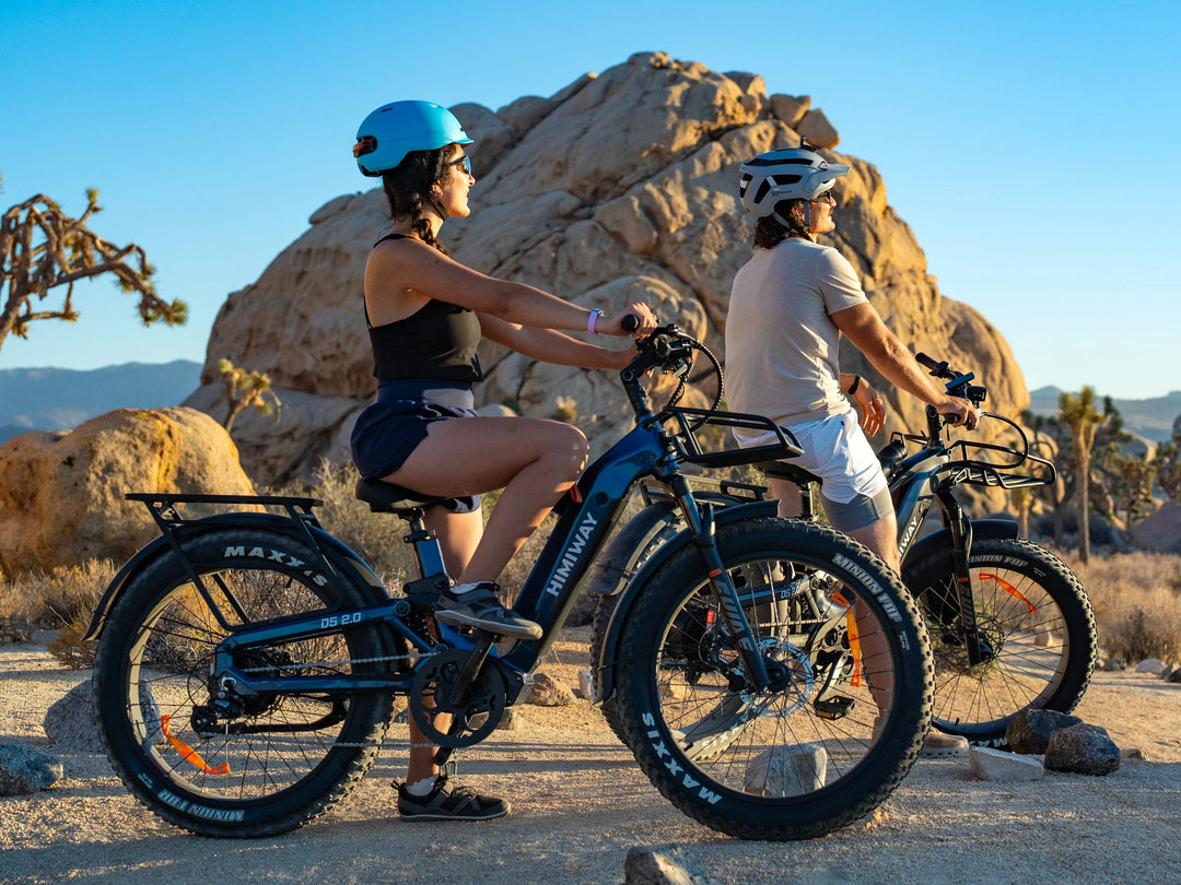 Two people riding electric bikes in a desert landscape with rocky formations.