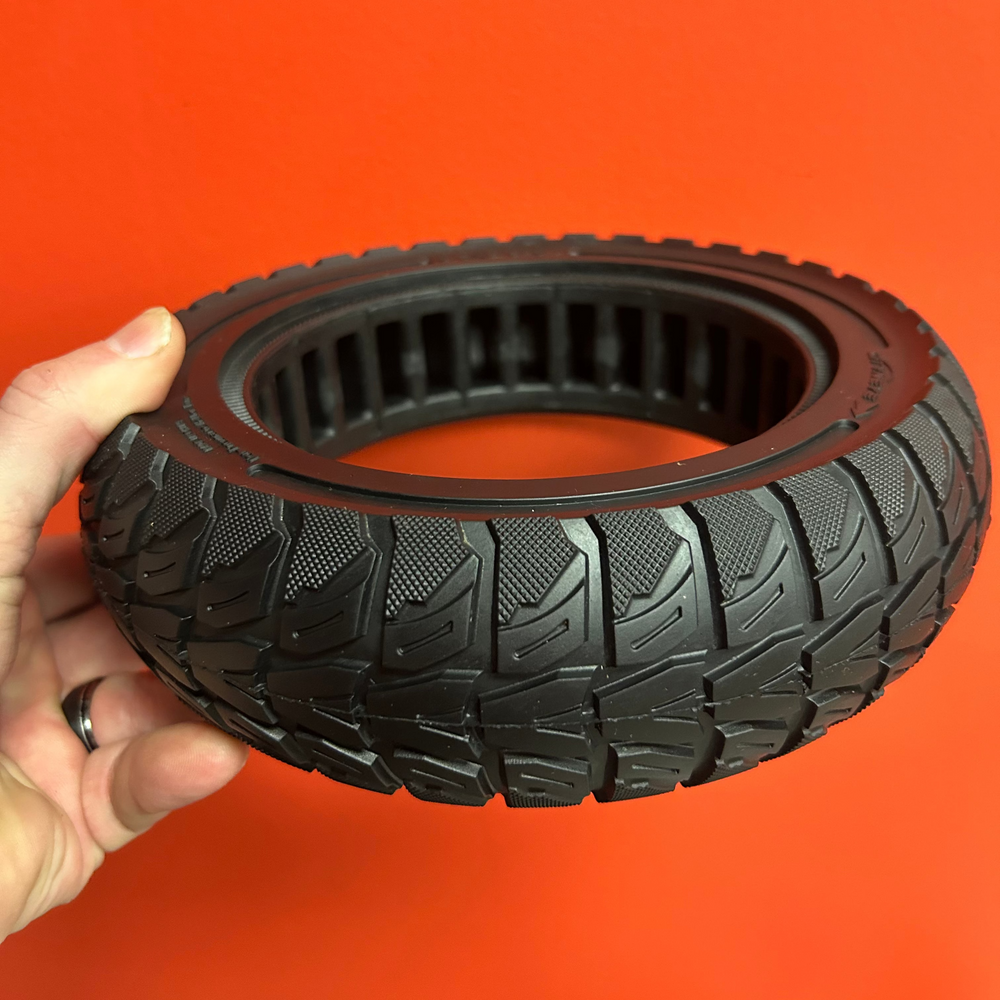 Hand holding a black tire against an orange background
