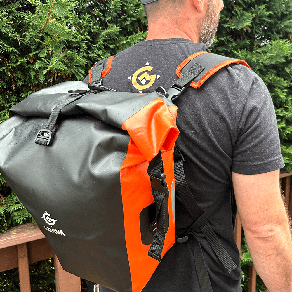 A person wearing the Grava Pannier Bag as a backpack, with the straps attached. The bag is securely worn on the person's back, offering convenience and versatility. The Grava logo and distinctive orange highlights are visible, adding a touch of style to the bag. This image showcases the multiple ways the Pannier Bag can be used, emphasizing its adaptability for different situations. Whether cycling or on foot, the bag transforms into a comfortable backpack, allowing for easy transportation of belongings.