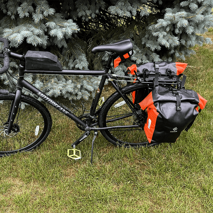 Pannier bags mounted on a bicycle rack. The Grava logo is prominently displayed on the bags, along with eye-catching orange highlights. The bags are securely fastened to the rack, showcasing their functionality and durability. This image captures the essence of the Grava Pannier Bags, highlighting their ability to provide reliable storage and enhance the biking experience.