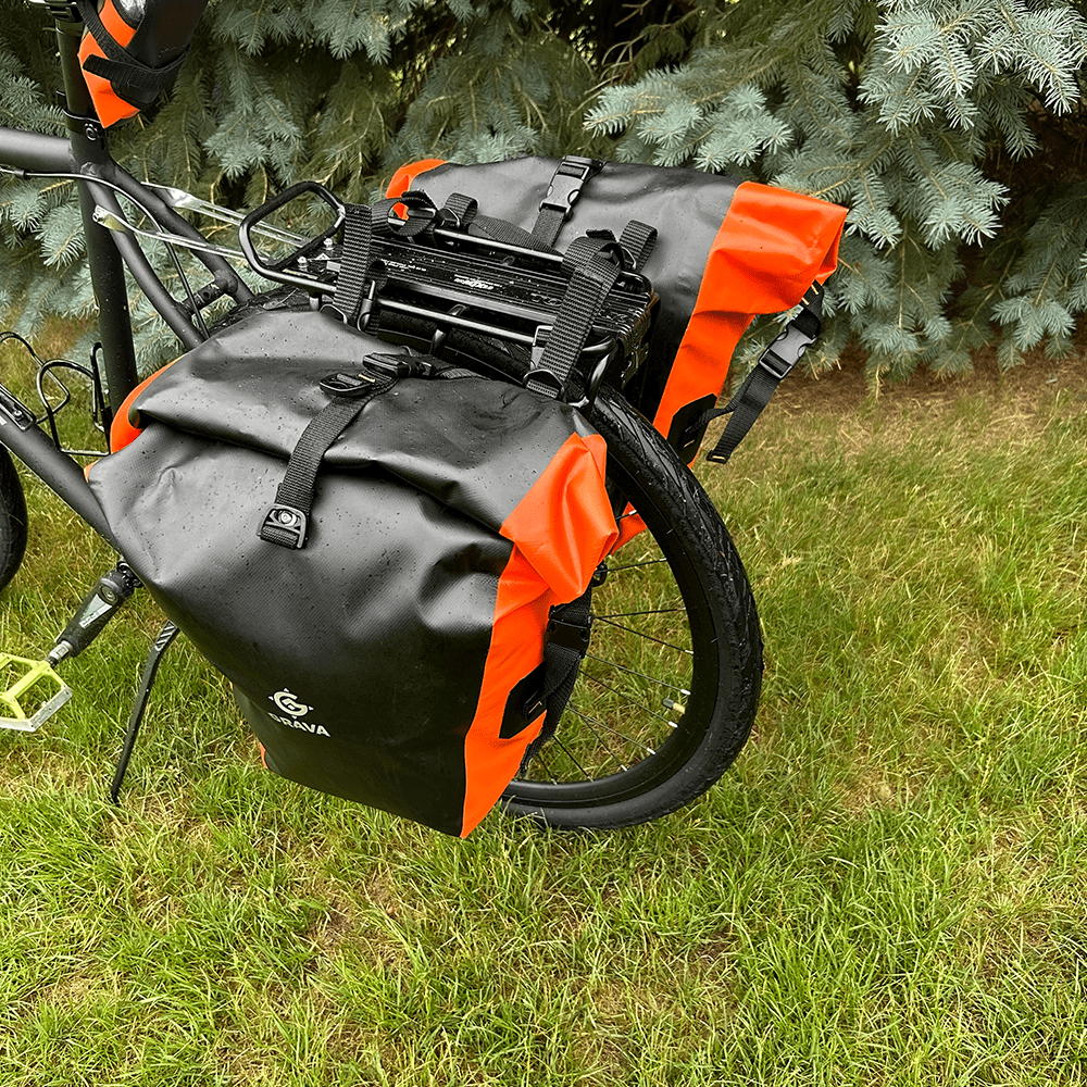 Pannier bags mounted on a bicycle rack. The Grava logo is prominently displayed on the bags, along with eye-catching orange highlights. The bags are securely fastened to the rack, showcasing their functionality and durability. This image captures the essence of the Grava Pannier Bags, highlighting their ability to provide reliable storage and enhance the biking experience.