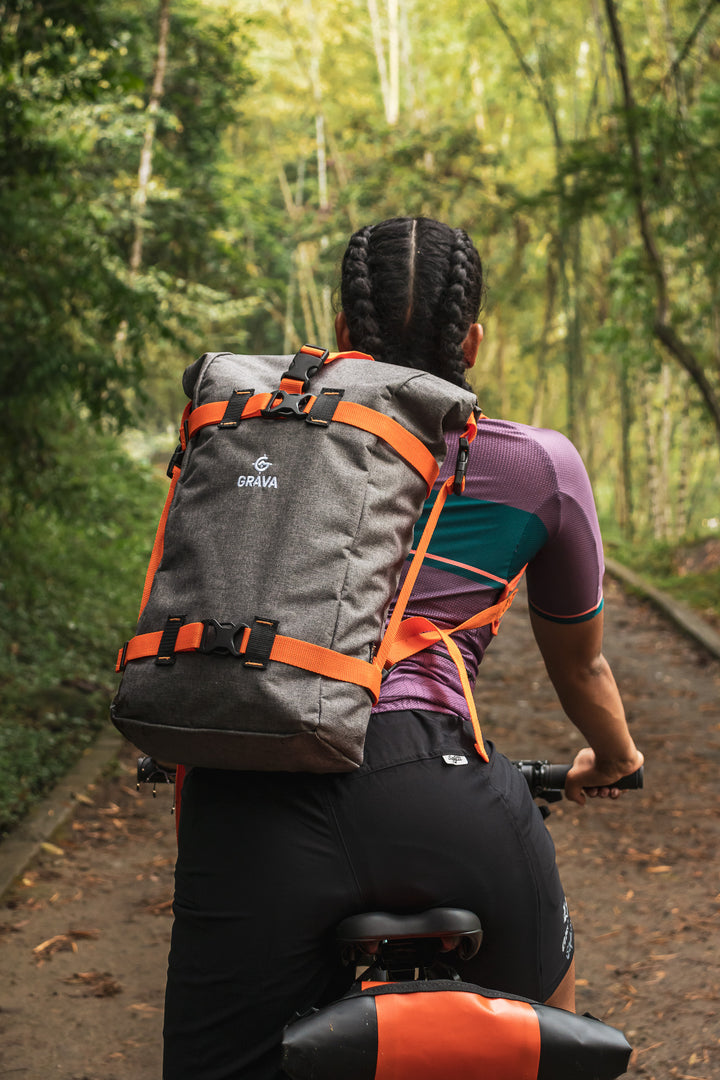 A bicycle rider confidently wearing the Grava Adventure Backpack while riding a bicycle. The backpack is securely fastened and prominently displayed on the rider's back. 