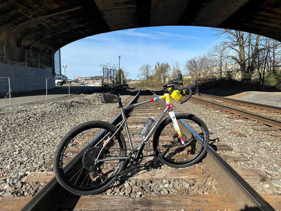 F. Duarte Stainless Steel bicycle in the colors of the Colombian flag sitting on RailRoad tracks.  You can see the beautiful stainless steel bicycle shining in the sunlight. 