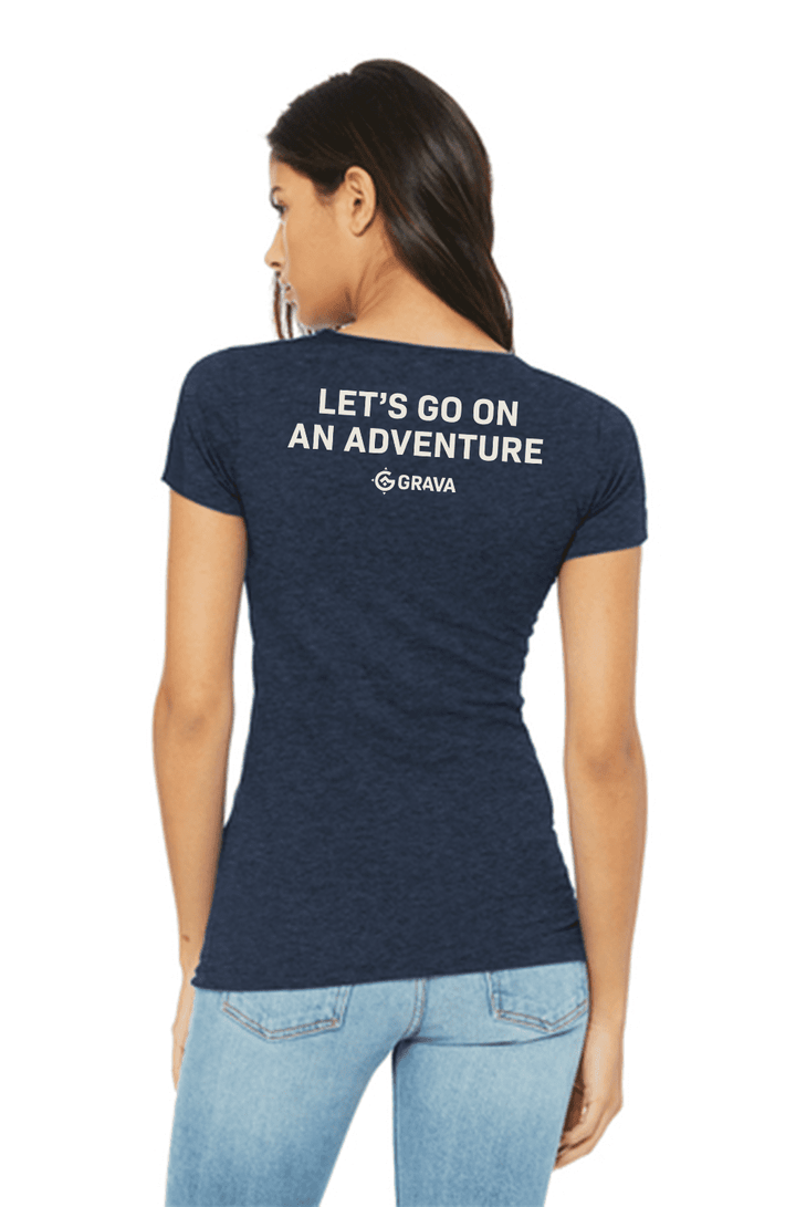 A woman wearing the Etcha Sketch Petite T-Shirt by Grava Adventure Corporation. The shirt features the iconic Grava logo with an etched terrain map in the background, evoking a sense of adventure and nostalgia. The woman is confidently sporting the t-shirt, which complements her casual and adventurous style.