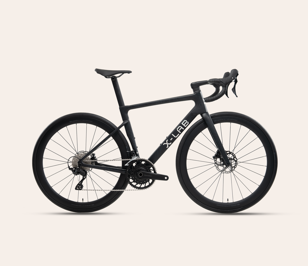 X-LAB RS7 Shimano 105 mechanical 12-speed road bike in Singularity Black, full bicycle drive-side view on a warm #F6EFE9 background