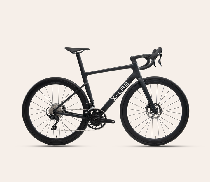 X-LAB RS7 Shimano 105 mechanical 12-speed road bike in Singularity Black, full bicycle drive-side view on a warm #F6EFE9 background